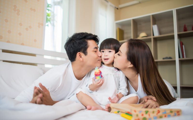 Happy child with parents playing in the bed at home