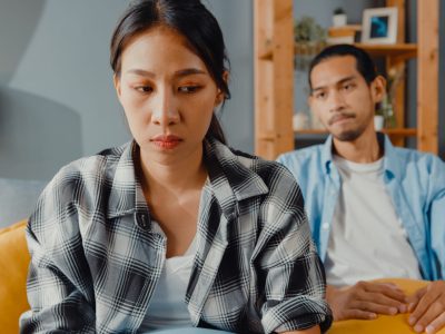 Upset asian couple wife sit on couch listen to furious husband yelling feel unhappy talk negative to her. Couple have fight or disagreement at home, Couple problem, family married toxic relationship.